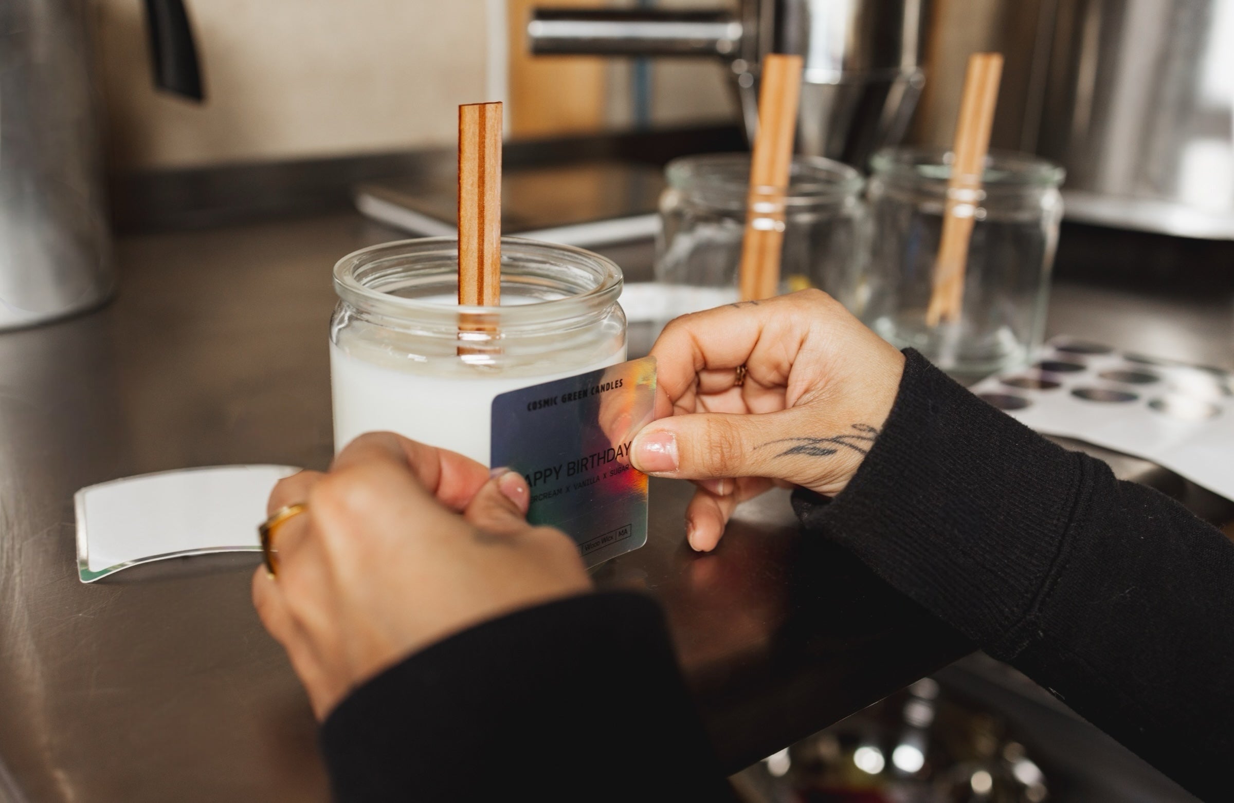 A close-up of hands placing a candle label on a jar, showcasing the craftsmanship and attention to detail in candle production.